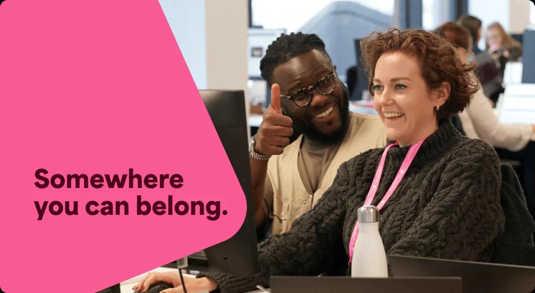 A photo of two Trustpilot employees smiling at their desk. The woman is looking at her laptop whilst the man is looking directly at the camera, giving a thumbs up gesture.